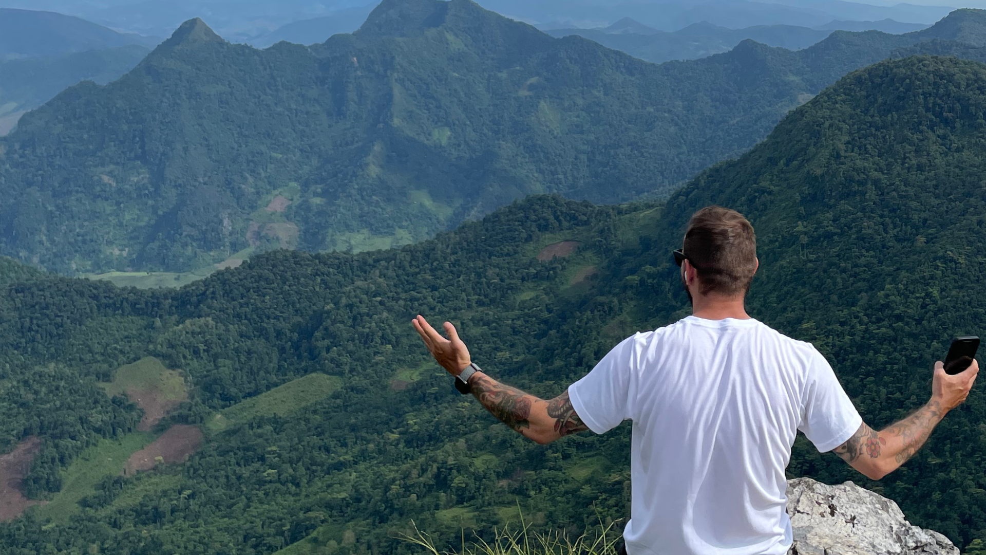 Chris with arms wide open on a mountain summit